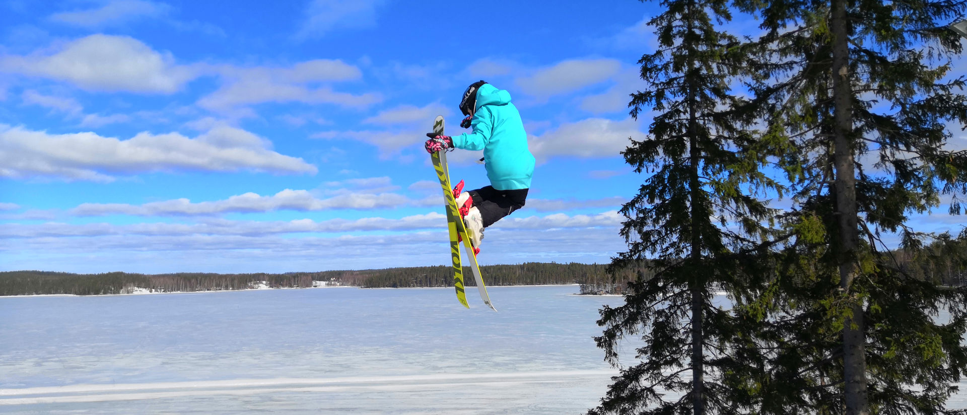 laskettelija hyppää hyppyristä, taustalla luminen järvimaisema